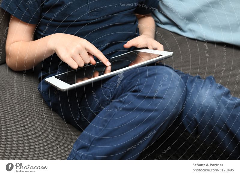 Kind sitzt auf der Couch mit einem Tablet auf dem Schoß und tippt mit einem Finger auf den Screen Neue Medien kind ipad Medienkonsum sitzen gemütlich Schule