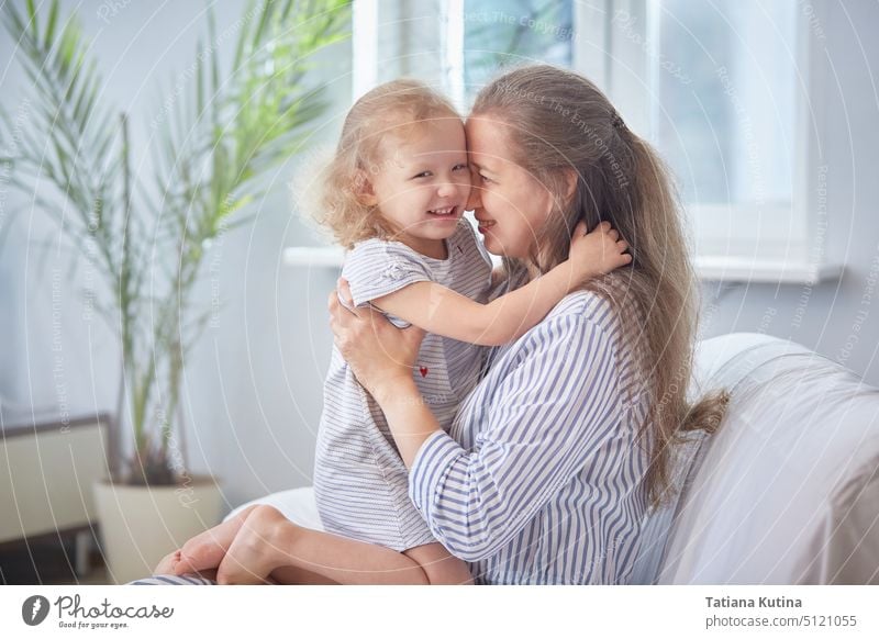 Alles Gute zum Muttertag. Mutter und Tochter sind lächelnd und umarmt auf dem Sofa zu Hause in einem hellen Raum. Das Konzept der Familie Glück mit Kindern. Familienurlaub und Zweisamkeit.