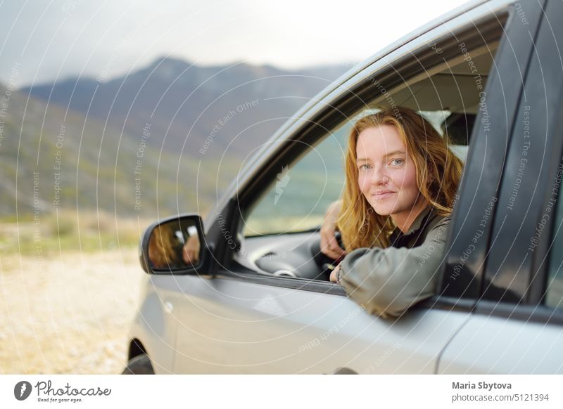 Eine junge, schöne, rothaarige Frau ist allein mit ihrem Auto unterwegs. PKW froh Fahrer Straße Ausflug Glück Miete Berge Mädchen Minivan reisen Tourist