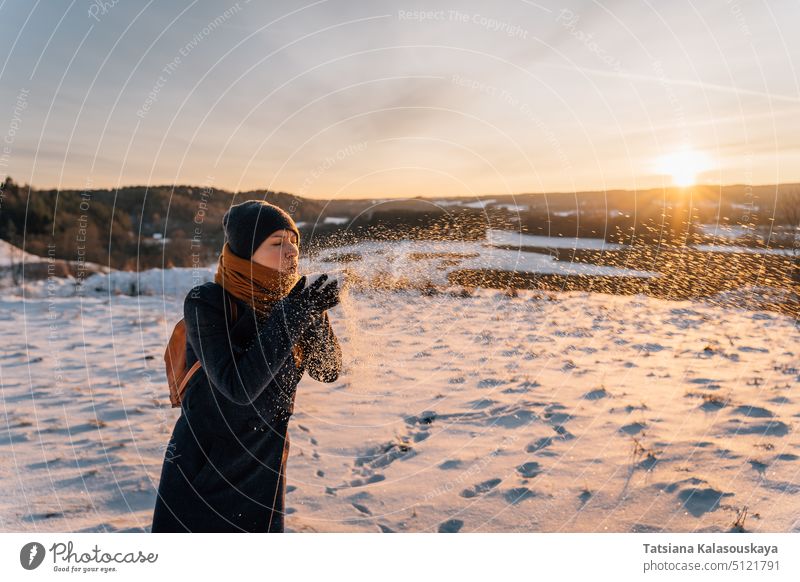 Eine Frau bläst bei Sonnenuntergang im Winter Schnee in ihre Handfläche Schlag warme Kleidung Menschen Person Europäer weiß Erwachsener mittlerer Erwachsener
