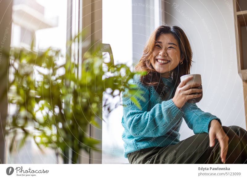 Junge Frau trinkt eine Tasse Kaffee in ihrer Wohnung echte Menschen offen Mädchen jung Erwachsener Spaß Jahrtausende Jahrtausendgeneration asiatisch Japanisch