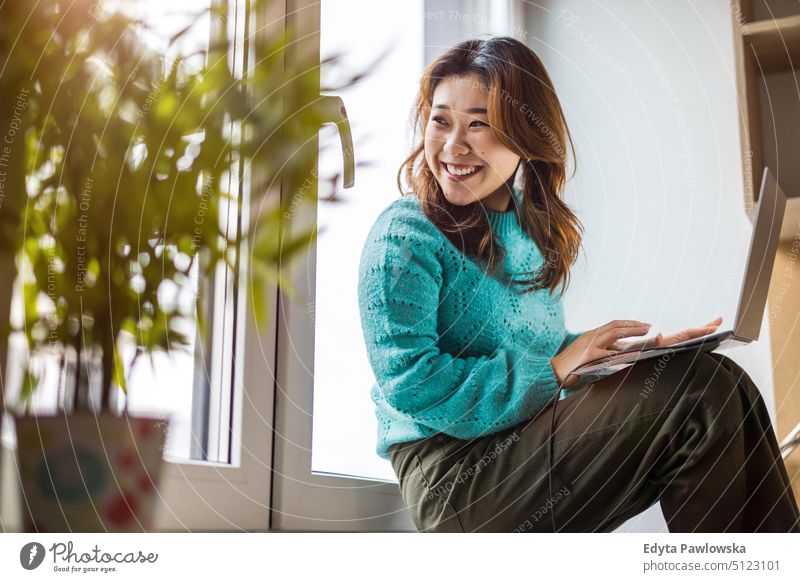 Junge Frau benutzt einen Laptop in ihrer Studiowohnung echte Menschen offen Mädchen jung Erwachsener Spaß Jahrtausende Jahrtausendgeneration asiatisch Japanisch
