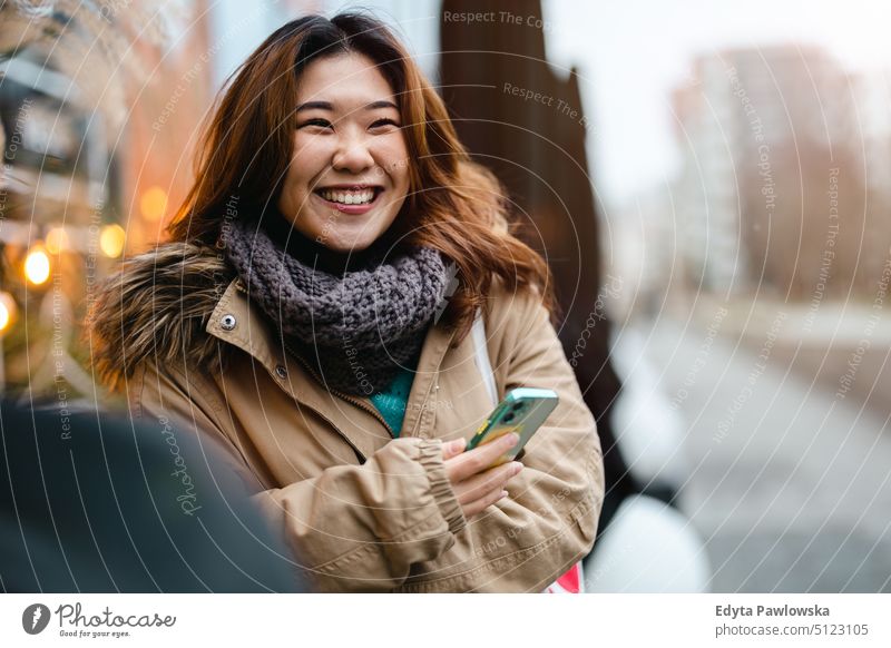 Junge Frau benutzt ein Mobiltelefon, während sie an der Bushaltestelle steht echte Menschen offen Mädchen jung Erwachsener Spaß Jahrtausende