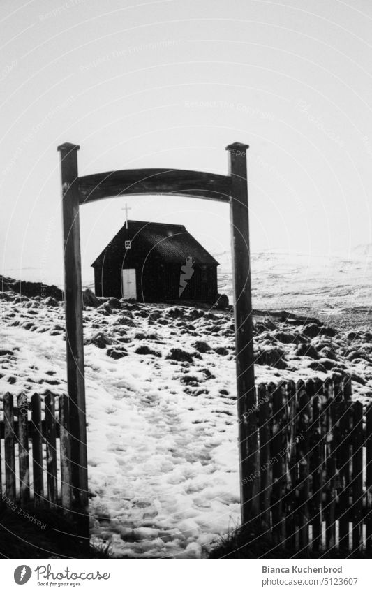 Fußspuren führen durch einen offenen Rahmen zu einer schwarzen Kirche in Island. Schwarzweißfoto Außenaufnahme Tag Religion & Glaube Menschenleer