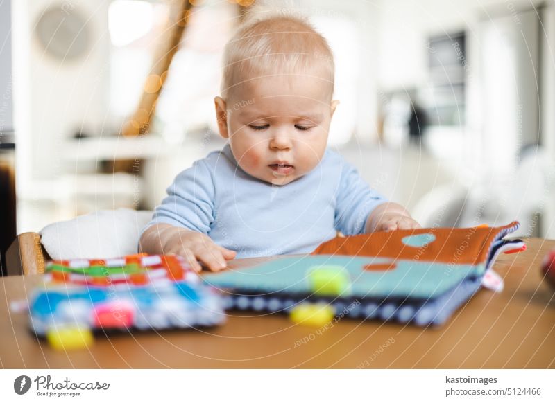 Glückliches Kleinkind sitzt am Esstisch und spielt mit seinem Spielzeug in traditionellen skandinavischen Designer-Holzstuhl in modernen hellen atic Hause. Niedliches Baby spielt mit Spielzeug