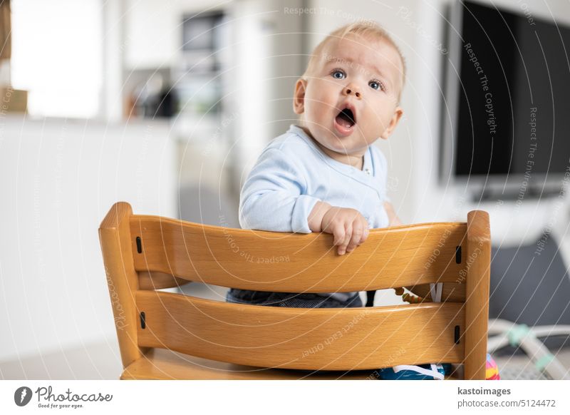 Kleinkind sitzt im traditionellen skandinavischen Designer-Hochstuhl aus Holz in einem modernen, hellen Haus. Niedliches Baby. Säugling Kind Glück niedlich