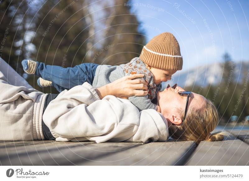 Glückliche Familie. Junge Mutter spielt mit ihrem kleinen Jungen Kleinkind im Freien auf sonnigen Herbsttag. Porträt von Mutter und kleinem Sohn auf Holzplattform am See. Positive menschliche Emotionen, Gefühle, Freude.