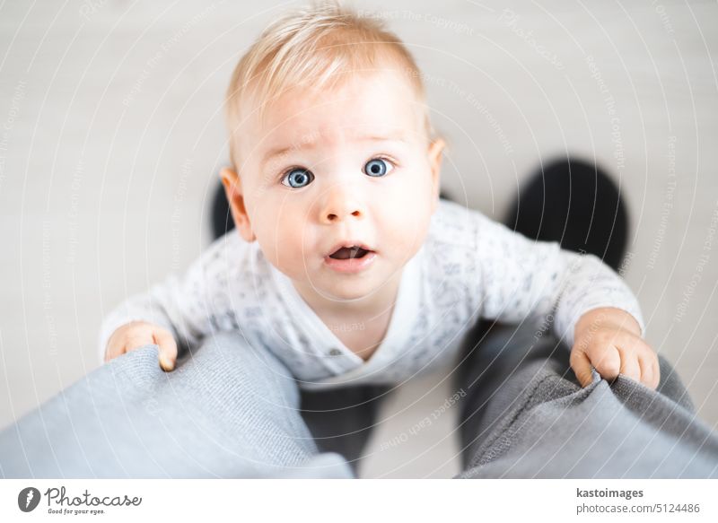 Draufsicht auf ein fröhliches Baby, das seine ersten Schritte macht und sich zu Hause an der Jogginghose seines Vaters festhält. Niedliches Baby Junge lernen zu gehen
