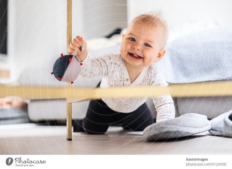 Cute Säugling Baby Junge spielt mit hängenden Ball, krabbeln und aufstehen von Wohnzimmer Tisch zu Hause. Baby-Aktivitäten und Spiel-Center für die frühe kindliche Entwicklung. Baby spielt zu Hause.