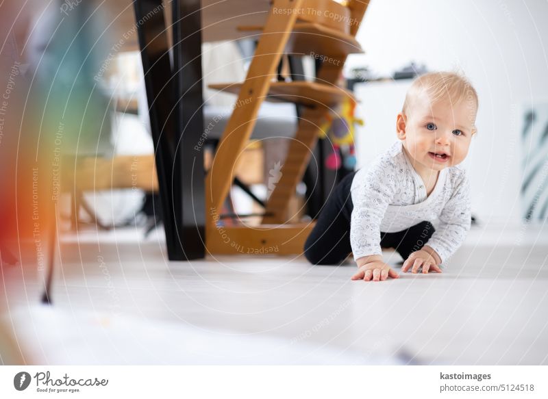 Cute Kleinkind Baby Junge krabbeln unter Esszimmer Tisch zu Hause. Baby spielt zu Hause neugeboren Porträt Säugling Blick spielen Kindheit Entwicklung Spielzeug