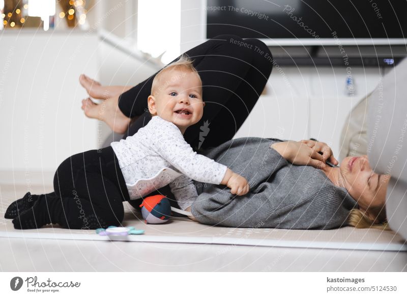 Glückliche Familienmomente. Mutter liegt bequem auf der Kindermatte und spielt mit ihrem kleinen Jungen, der seine ersten Schritte beobachtet und überwacht. Positive menschliche Emotionen, Gefühle, Freude.