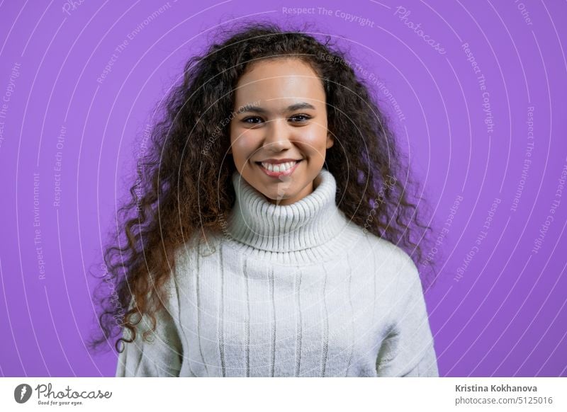 Porträt einer hübschen Frau auf violettem Studiohintergrund. Positives junges Mädchen mit natürlichem lockigem Haar, sie im weißen Pullover lächelt in die Kamera.