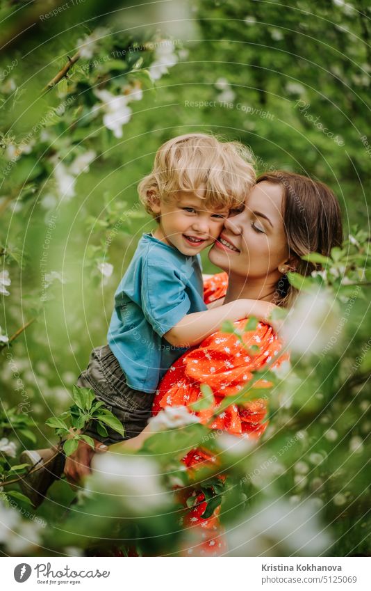 Schöne rührende Szene von Mutter und Kleinkind Sohn in blühenden Frühlingsgarten. Glückliche Mutter und Baby Junge umarmt. Familie, Liebe, Kindheit Konzept.
