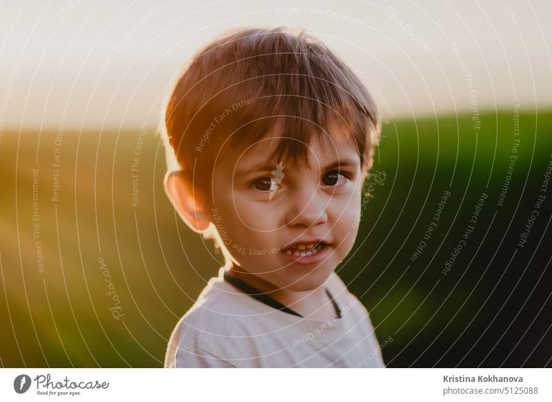 Porträt eines lächelnden Kindes, das auf einer frischen grünen Wiese steht. Lovely Kleinkind Junge erforscht Pflanzen, Natur im Frühling. Kindheit, Zukunft, Landwirtschaft, Ökologie Konzept