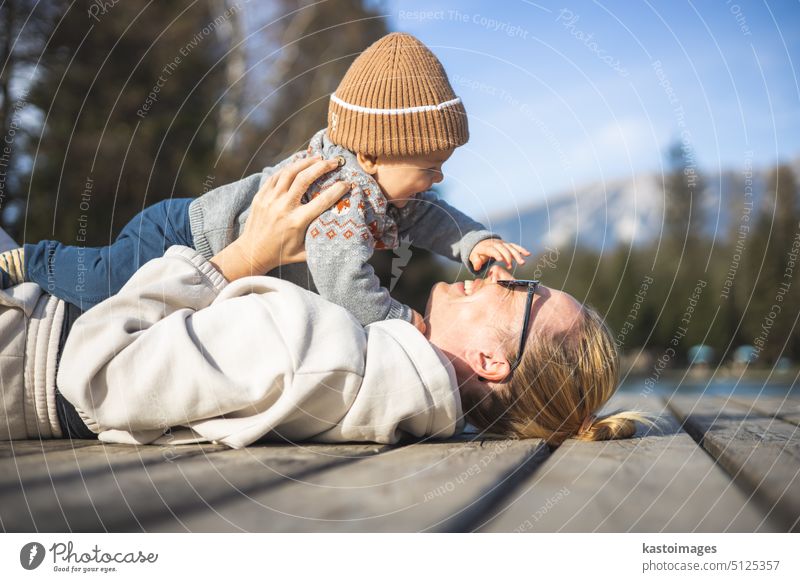 Glückliche Familie. Junge Mutter spielt mit ihrem kleinen Jungen Kleinkind im Freien auf sonnigen Herbsttag. Porträt von Mutter und kleinem Sohn auf Holzplattform am See. Positive menschliche Emotionen, Gefühle, Freude.