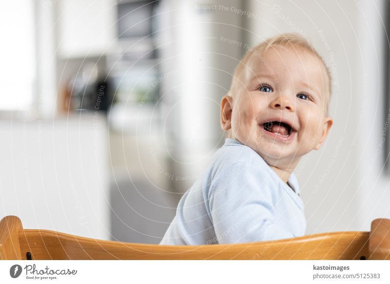 Happy Kleinkind sitzt in traditionellen skandinavischen Designer-Holz-Hochstuhl und lachen laut in modernen hellen Haus. Niedliches Baby-Lächeln. Säugling Kind
