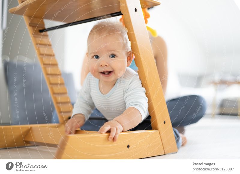 Glückliches Kleinkind klettert unter traditionellen skandinavischen Designer-Holzstuhl und in modernen hellen Haus. Niedliches Baby lächelt in die Kamera