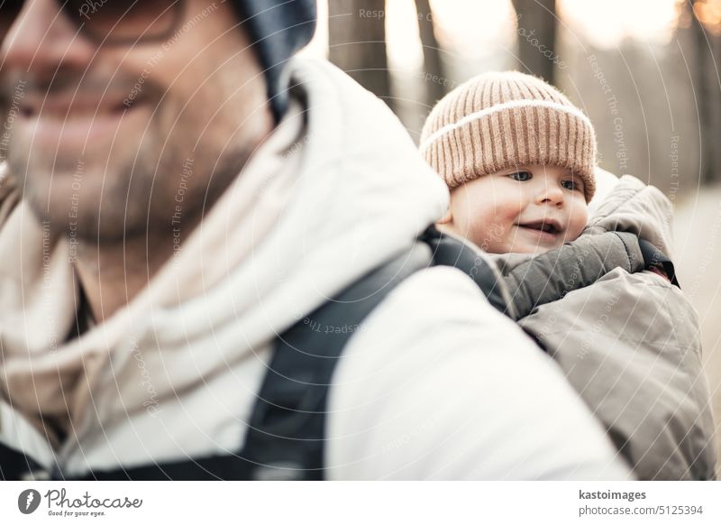 Sportlicher Vater, der seinen kleinen Sohn im Winterpullover und mit Mütze im Rucksack auf dem Rücken durch den Herbstwald trägt. wandern Säugling Träger reisen
