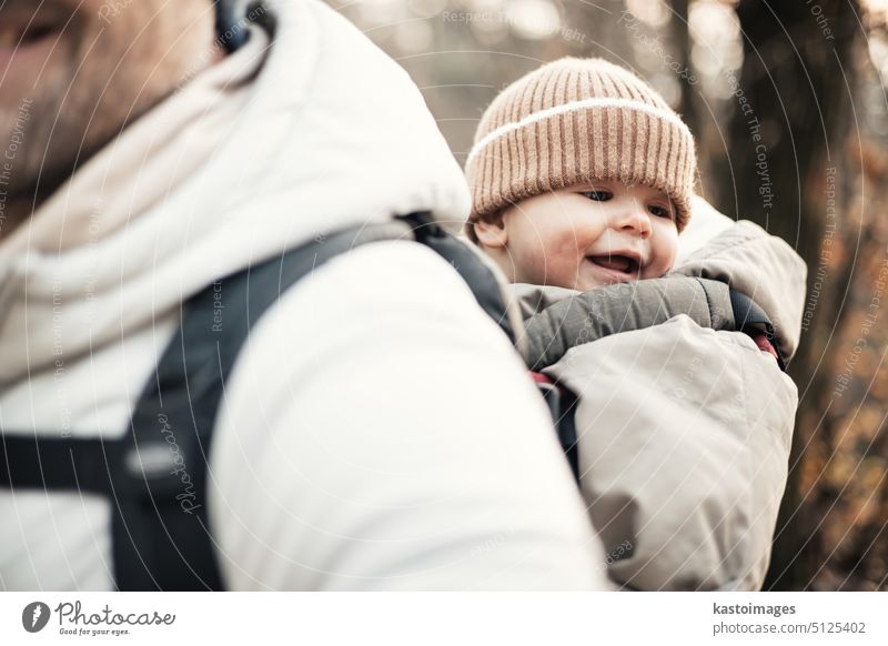 Sportlicher Vater, der seinen kleinen Sohn im Winterpullover und mit Mütze im Rucksack auf dem Rücken durch den Herbstwald trägt. wandern Säugling Träger reisen