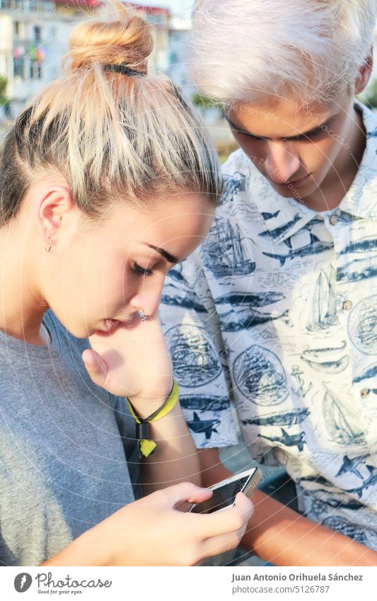 Mädchen tippt auf ihrem Mobiltelefon, während ein Junge sie ansieht Jugendzeit Menschen jung Jugendlicher gutaussehend geschnitten Teenager lässig Porträt