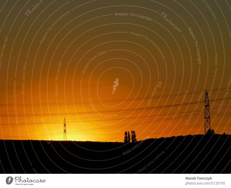 Rötlichgelber Sonnenuntergang hinter Hochspannungsleitungen und Hochspannungsmasten. Abenddämmerung Horizont Stromtransport Überlandleitung Stromtrasse