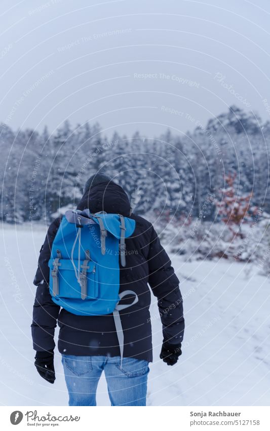 Rückansicht von einem Mann mit einem blauen Rucksack im Schneefall schneien Winter kalt winterlich Winterstimmung Schneeflocken Schneegestöber Außenaufnahme