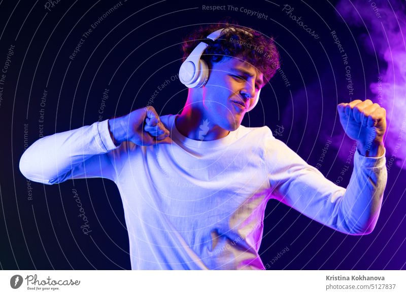 Positiver Mann hört Musik mit Kopfhörern, tanzt auf dunklem Neon-Hintergrund. Stilvolle Student Kerl genießt das Leben, aktive Energie, inspiriert Tanz Konzept