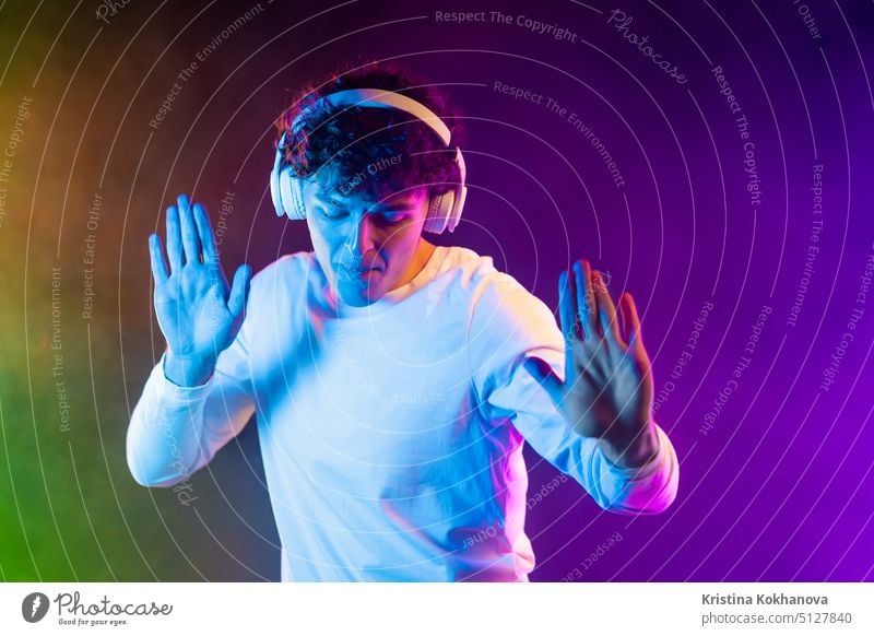 Positiver Mann hört Musik mit Kopfhörern, tanzt auf dunklem Neon-Hintergrund. Stilvolle Student Kerl genießt das Leben, aktive Energie, inspiriert Tanz Konzept