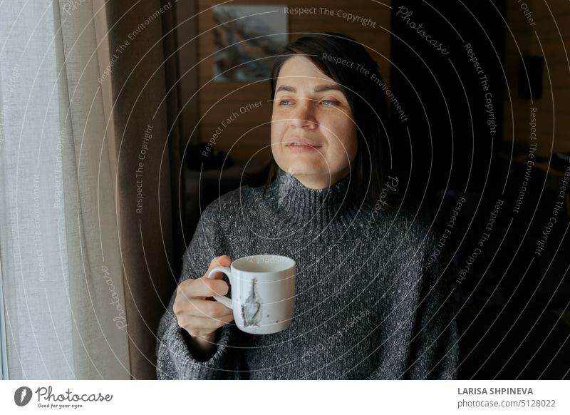 Porträt einer nachdenklichen Frau. Mädchen mit Tasse Kaffee. Frau trinkt Tee zu Hause am Fenster trinken weiß Getränk heiß Becher Schönheit Menschen Person Café