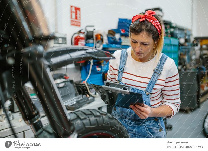 Mechaniker, der Informationen über ein Motorrad in der Werkstatt überprüft Frau überblicken Dokumentation Überprüfung Checkliste Garage Fabrik Konzentration