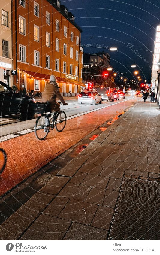 Eine Fahrradfahrerin fährt nachts auf dem Fahrradweg neben Autos durch die Stadt dunkel Straße Verkehr Fahrzeug Mobilität Bewegung Ampeln Verkehrsmittel