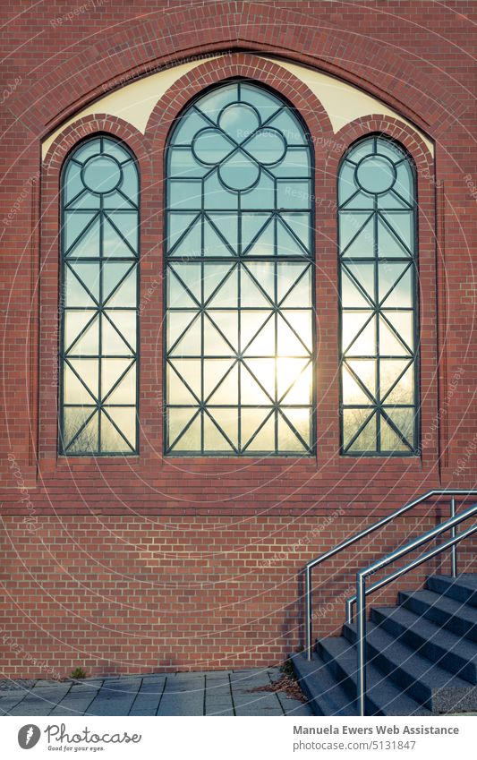 Eine Ziegelstein-Fassade mit verzierten Fenstern, die die untergehende Sonne spiegeln. spiegelndes fenster fensterfassade sonne hoffnung ziegelstein ziegelmauer