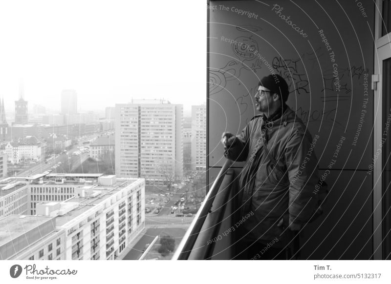 Mann mit Mütze redet auf einem Balkon mit Ausblick auf Berlin Mitte ausblick s/w Plattenbau Schwarzweißfoto Außenaufnahme Tag Architektur Stadt Stadtzentrum