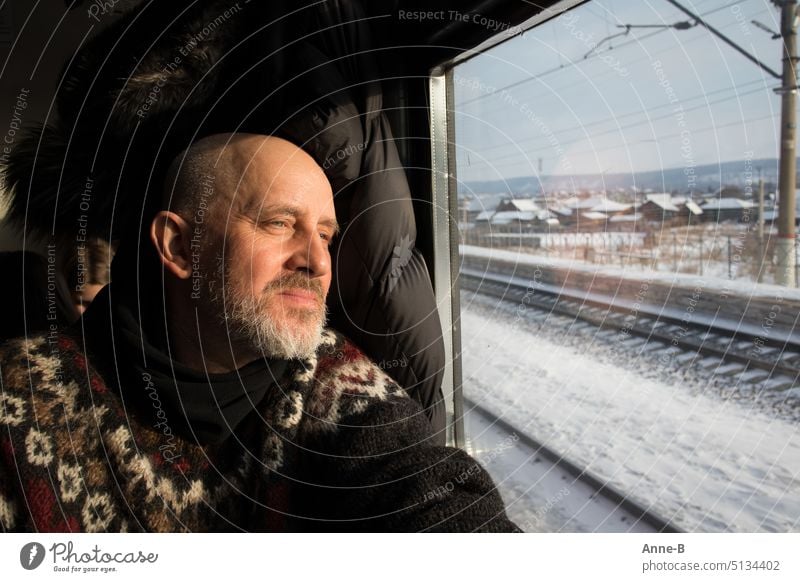 Mann sitzt im Strickpullover im Zug und schaut aus dem Fenster in den sonnigen sibirischen Winter bahn bahnfahrt zugfenster rausschauen winter strickpullover