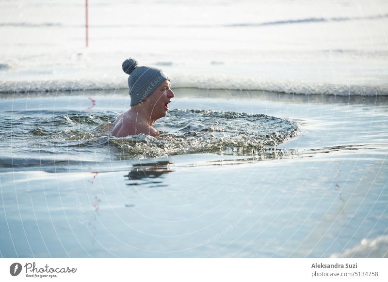 Ein Mann mit warmer Mütze schwimmt in einem Eisloch. Winteraktivitäten in Finnland. Gesunder Lebensstil Aktivität Erwachsener alternativ Baden Körper Pflege