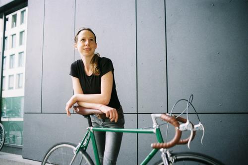 Junge Frau mit grünem Vintage-Rennrad vor grauer Wand vintage Singlespeed urban Textfreiraum links Mobilität retro Lifestyle Fahrrad Verkehrsmittel sportlich