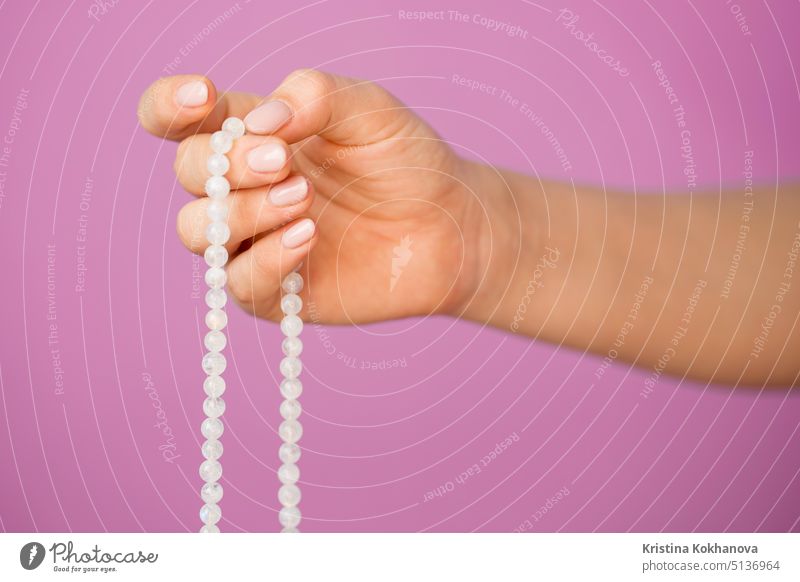 Frau, beleuchtete Hand aus der Nähe, zählt Malas, Stränge von Edelsteinperlen, die zum Zählen während Mantra-Meditationen verwendet werden, auf rosa Hintergrund