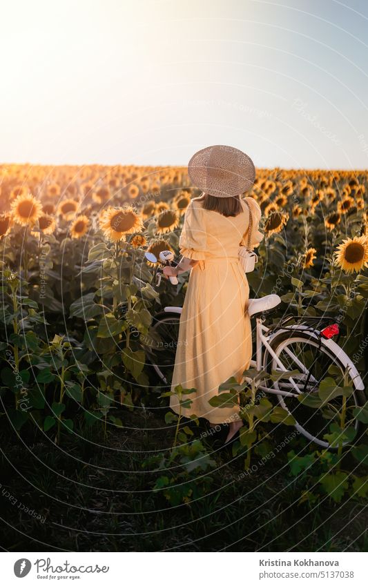 Attraktive Frau in zeitlosem Kleid mit Fahrrad im Retro-Stil im Sonnenblumenfeld. Vintage-Mode, erstaunliche Abenteuer, Aktivitäten auf dem Land, gesunder Lebensstil.