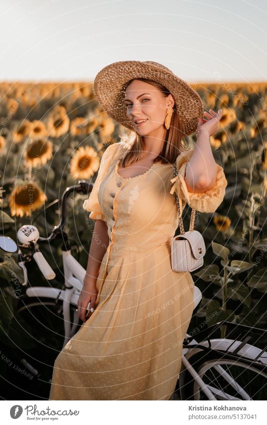 Attraktive Frau in zeitlosem Kleid mit Fahrrad im Retro-Stil im Sonnenblumenfeld. Vintage-Mode, erstaunliche Abenteuer, Aktivitäten auf dem Land, gesunder Lebensstil.