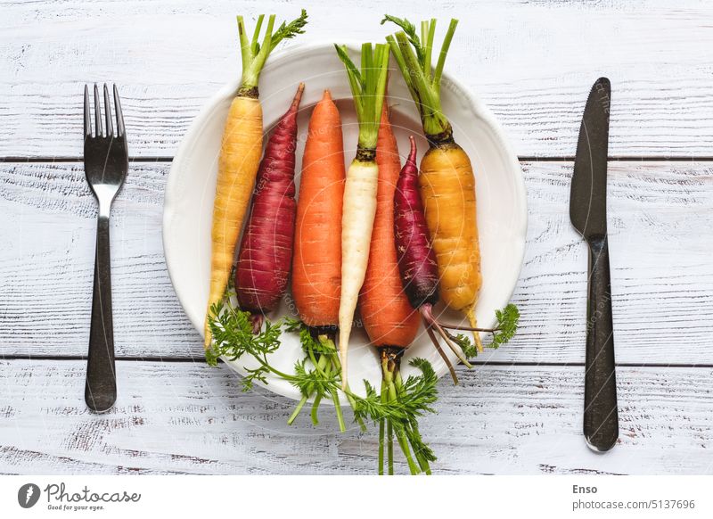 Regenbogenkarotten auf Teller, Besteck auf Holztisch, Draufsicht Karotten Farbe verschiedene mehrfarbig purpur weiß gelb orange frisch gepflückt Essen Gabel