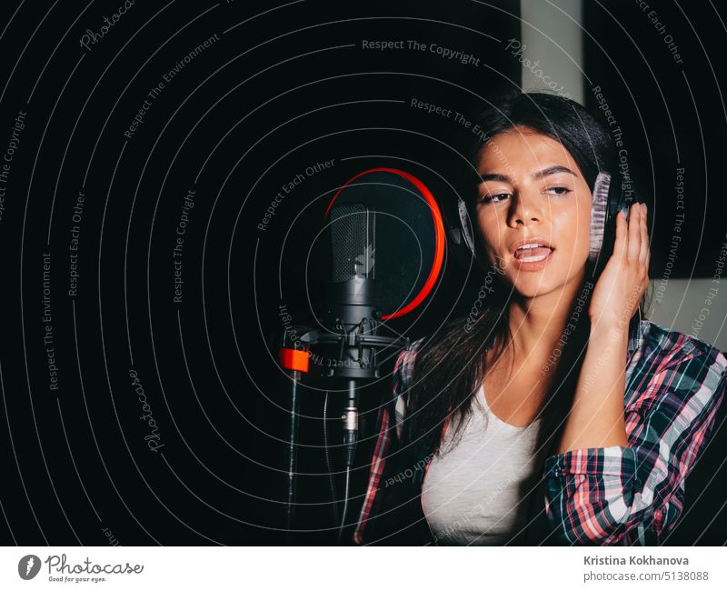 Junge schöne brünette Frau Aufnahme Stimme, Song oder Album in professionellen Studio. Mädchen singt in der Nähe von Mikrofon im Aufnahmeraum unter natürlichem Licht.