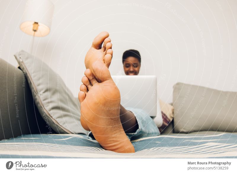 Nahaufnahme Füße einer schwarzen Frau, die ihren Laptop auf einer Couch benutzt 20s Erwachsener Barfuß schön Bett Schlafzimmer Schnappschuss Pflege lässig