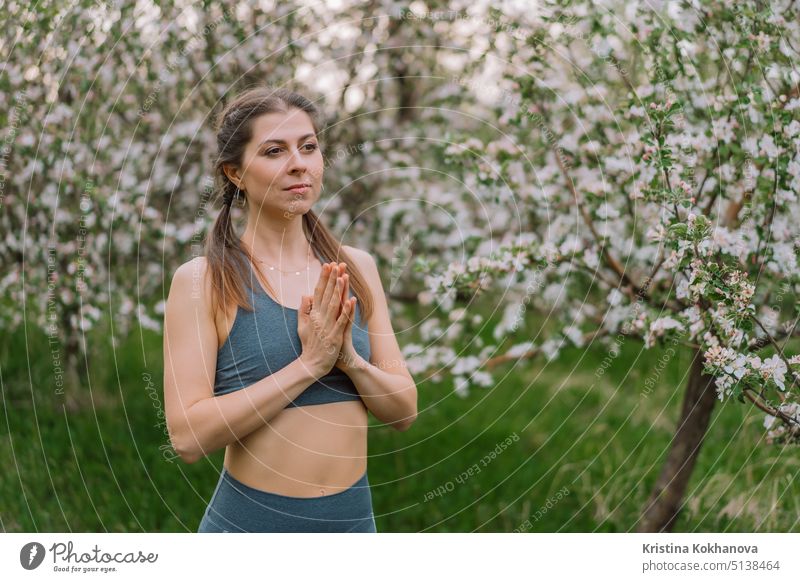 Frau mit Namaste Yoga Mudra Hände auf Frühlingsblüten Garten natürlichen Hintergrund. Gesundes Mädchen Training an der frischen Luft. Dankbarkeit, Einheit mit der Natur, Frieden und Liebe Konzept.