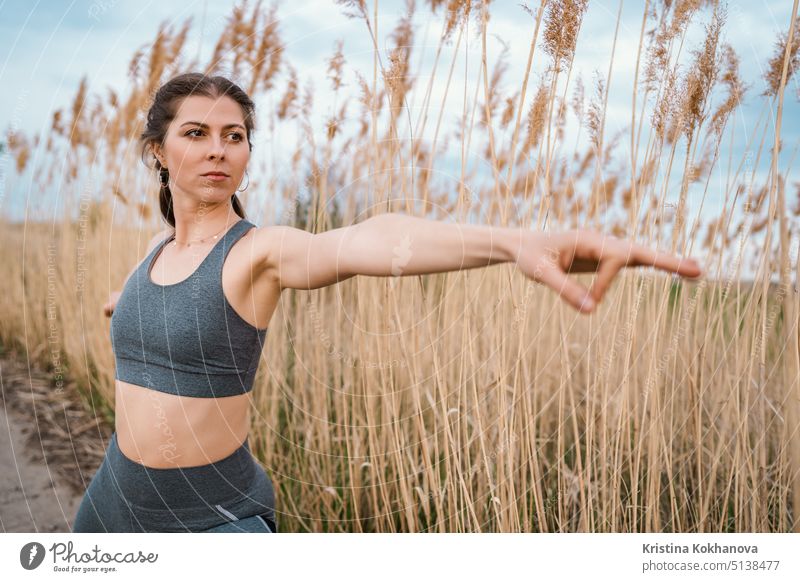 Europäische Frau macht Yoga-Übung auf Schilf natürlichen Hintergrund. Konzentrierte Mädchen Training im Sommer im Freien. Pastellfarben, Einheit mit der Natur, Gleichgewicht, Lifestyle-Konzept.