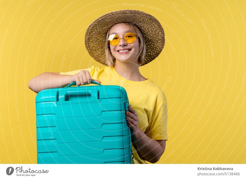Junge hübsche Frau mit Handgepäckkoffer auf gelbem Hintergrund. Teenager-Reisen mit blauen Gepäcktasche für Flugzeug Handgepäck. Sommerreise, Urlaub Konzept.