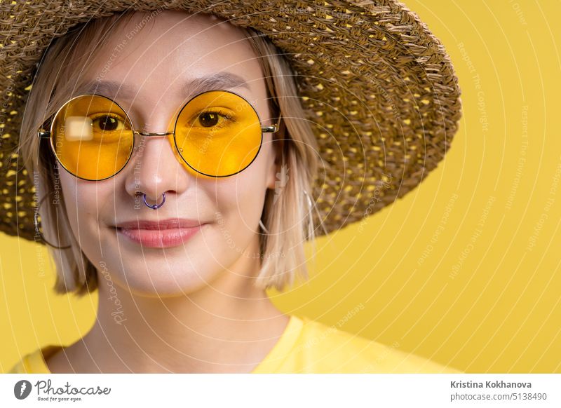 Porträt einer jungen hübschen blonden Frau auf sommerlichem gelben Studiohintergrund. Selbstbewusstes sonniges Outfit mit Sonnenbrille und Strohhut. Erwachsener