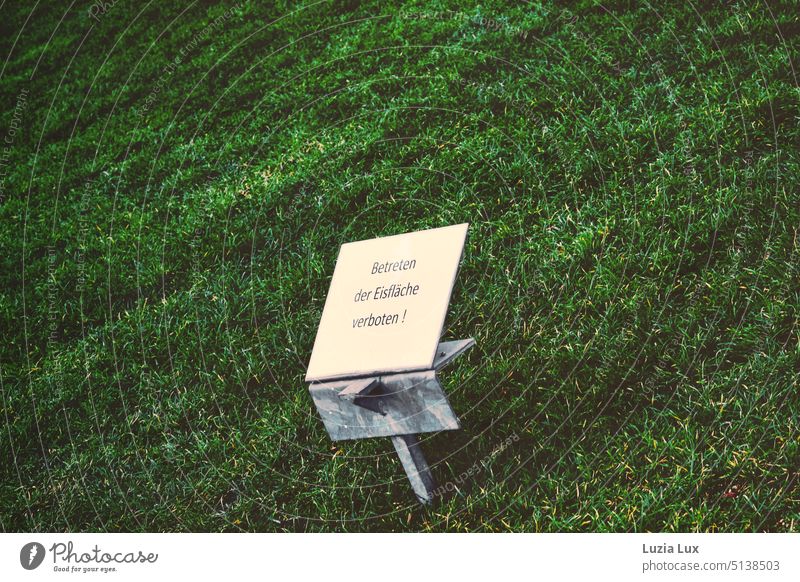Symbol des Klimawandels: Schild 'Betreten der Eisfläche verboten!' steht auf einer grünen Wiese Schilder & Markierungen Winter Winterstimmung Rasen grüne Wiese