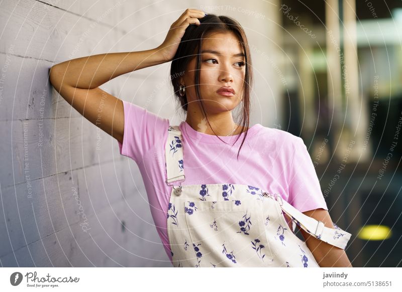 Stilvolle asiatische Frau lehnt an der Wand fettarm Windstille Straße urban modern Tastkopf Persönlichkeit jung ethnisch T-Shirt gesamt friedlich feminin