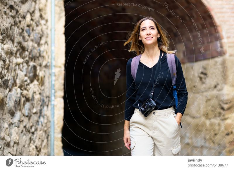 Positiv gestimmte Frau lächelt bei der Besichtigung der alten Stadt im Urlaub Sightseeing Tourist Lächeln Spaziergang Torbogen Glück bewundern Ausflug Reisender