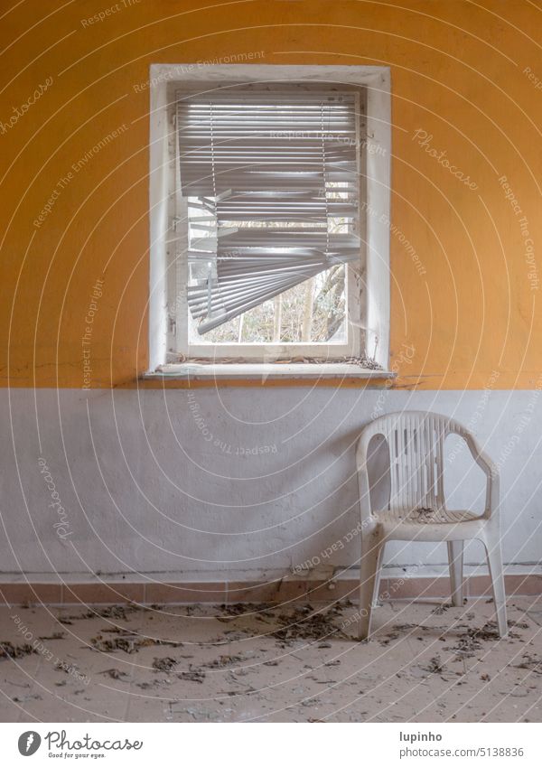 Plastikstuhl vor einem Fenster mit heruntergelassener Jalousie orangeweiß Wand lostplace Bauernhaus Bayern Innenraum Blätter alt verlassen spinnweben stuktur